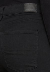 Mustat denim-farkut, joissa on sileä rakenne ja hillitty tikkaus. Sisältää takataskun ja nahkainen brändilappu, jossa lukee "AMERICAN EAGLE."