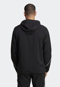 Černá kapucňová bunda s hladkou texturou, s bílými postranními akcenty a volným střihem. Na zadní straně odhaluje design nastavitelných kapucí.