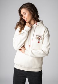 Lichte beige hoodie met de grafische opdruk "NIET MIJN CIRCUS", rode accenten en ribgebreide manchetten en zoom. Soepele stof en een detail van een voorzak.