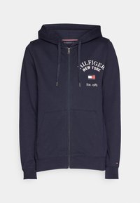 Sweat à fermeture éclair bleu marine en mélange de coton, avec un logo imprimé à l'avant, des poches kangourou et une capuche avec cordon de serrage. Détails en côtes aux poignets et à l'ourlet.