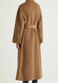 Cappotto di lana marrone con vita cinturata, maniche lunghe e silhouette dritta. La consistenza è morbida, con una lunghezza fino a metà coscia.