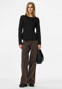 Czarna bluzka z długim rękawem i dopasowanym wcięciem w talii, połączona z brązowymi spodniami o szerokich nogawkach i czarnymi butami na platformie, trzymając czarną skórzaną torbę.