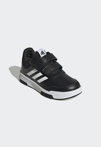 Scarpa sportiva nera con tomaia sintetica testurizzata, tre strisce bianche e strap in velcro. Presenta una suola in gomma con un motivo di trazione e un logo.