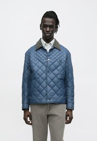 Gesteppte blaue Jacke mit einem grauen Kragen, ausgestattet mit einem Druckknopfverschluss und Seitentaschen. Glatte Textur und Steppmuster in Rautenform.