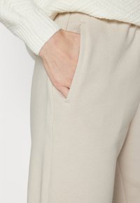 Beige vidde bukser med en glatt bomullsblanding, som har sidelommer og en avslappet passform. Stoffet har en subtil tekstur.
