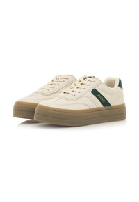 Zapatillas con cordones en crema con acentos verde oscuro, que cuentan con un upper sintético suave y una suela de goma beige gruesa. Líneas de diseño clásico.