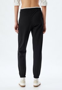 Zwarte tapered joggers met een elastische tailleband, opgerolde enkels en een soepele stofstructuur, gecombineerd met witte sneakers en sokken.