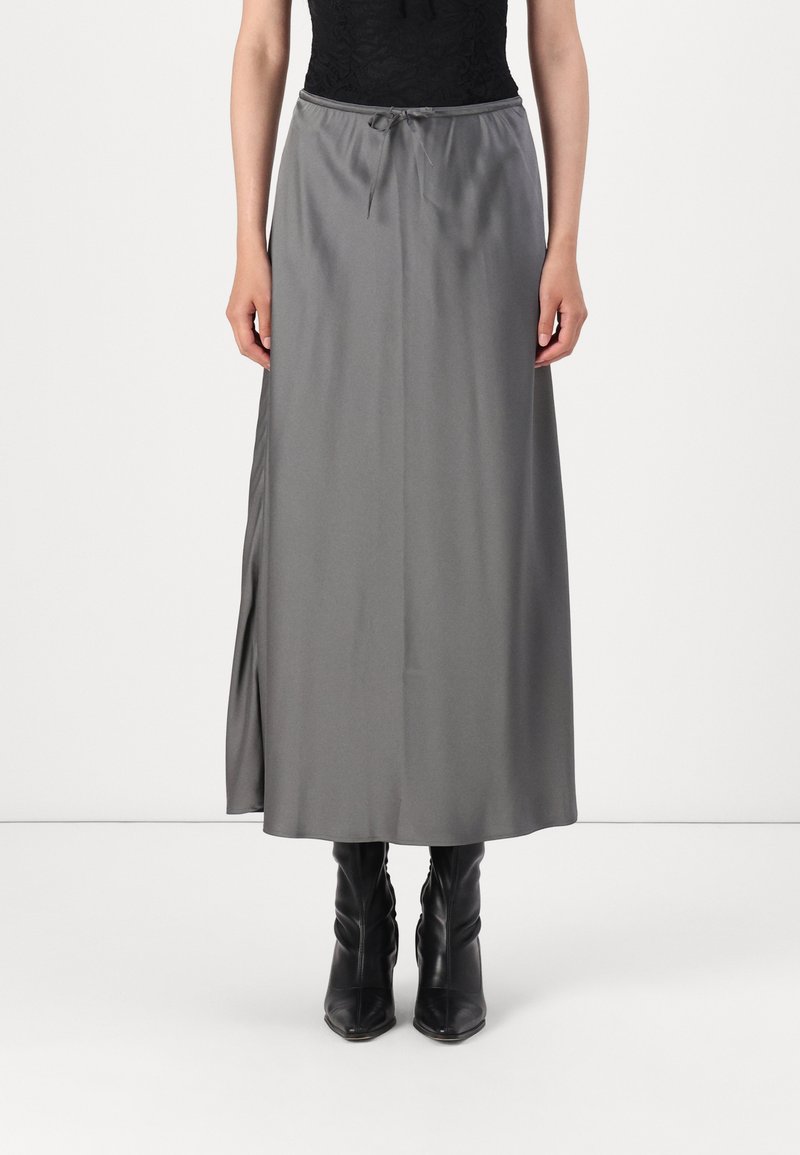 Gray satin maxi skirt with an elastic waistband and a tie detail, featuring a side slit. Worn with black, heeled, ankle-length boots.