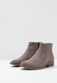 Gray suede ankle boots with a zipper, rounded toe, textured side panels, and a low stacked heel for comfort and stability.