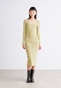 Long-sleeve knit dress in pale green with a square neckline, featuring vertical ribbed texture and a body-hugging silhouette. Paired with black boots.