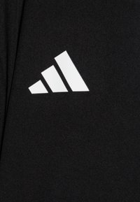 Svart atletisk tyg har en vit tre-stripes logotyp i en diagonalt mönster, vilket betonar en ren och modern design.