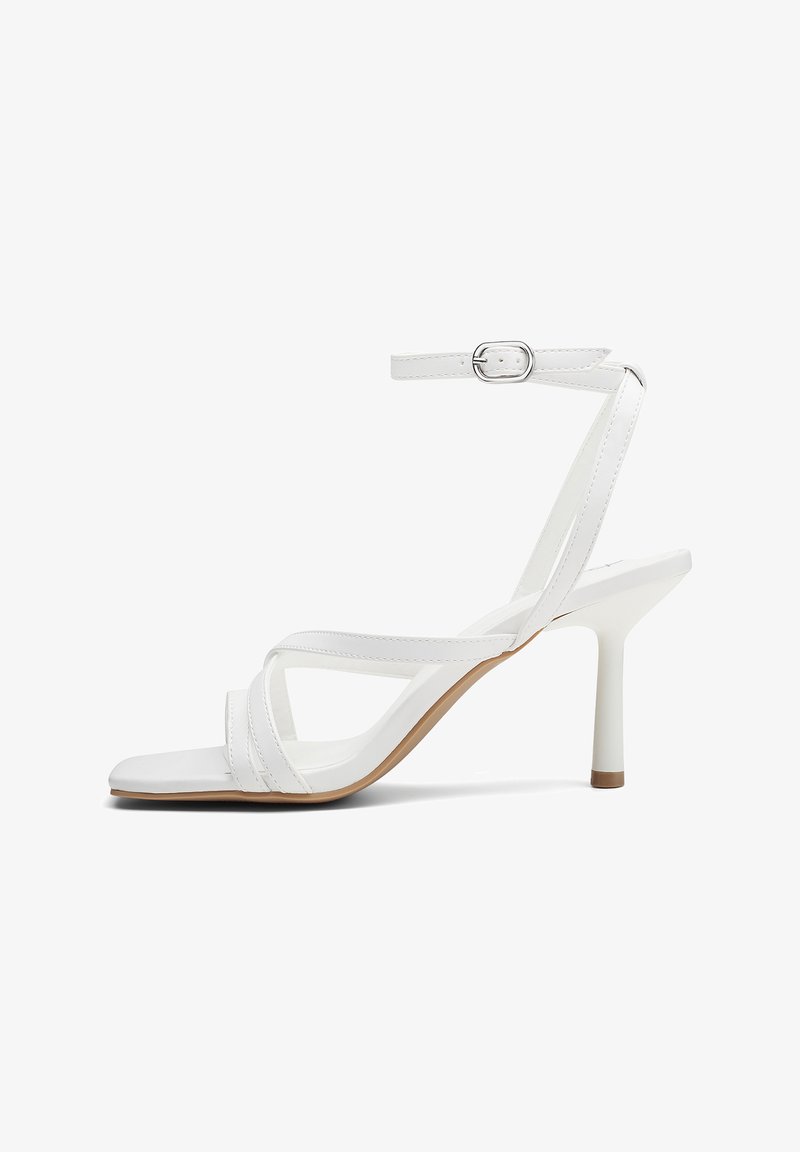 Sandali con tacco alto bianchi e a strappo, dotati di un sottile cinturino alla caviglia e un design a punta quadrata. Realizzati in materiale sintetico liscio con suola marrone.