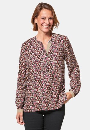 Long-sleeve blouse in a patterned fabric featuring circular shapes in shades of beige, burgundy, and red. Includes a partial button placket.