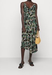 Černé šaty s řetízkovým vzorem v zelené, růžové a bílé barvě. Mají drapovaný výstřih a midi délku, doplněné černými sandály na podpatku.