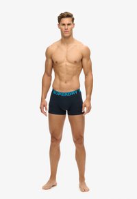 Czarne bokserki z niebieską gumką "SUPERDRY", wykonane z miękkiego, elastycznego materiału. Design jest dopasowany z średnim stanem.
