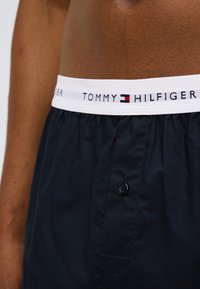 Σκούρα μπλε ανδρικά εσώρουχα boxer με λευκή ελαστική μέση που φέρει το λογότυπο "TOMMY HILFIGER" και ένα κουμπί εμπρός κλείσιμο.