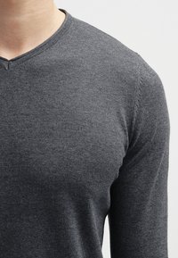 Camiseta gris de manga larga con diseño de cuello en V, textura suave y detalles sutiles de costuras en los hombros y los laterales.