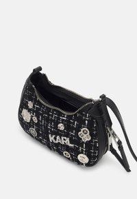 Sac à main en tweed noir avec des accessoires en métal argenté. Fermeture éclair et logo détaillé. Surface texturée avec des boutons décoratifs.