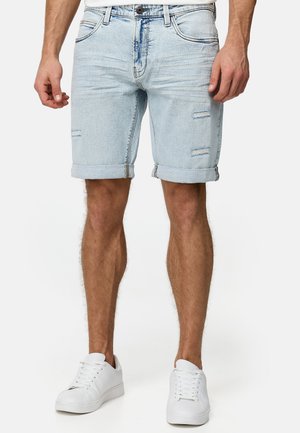 Light blue denim shorts with rolled cuffs, featuring distressed detailing, five pockets, and a button closure. Worn with white sneakers.