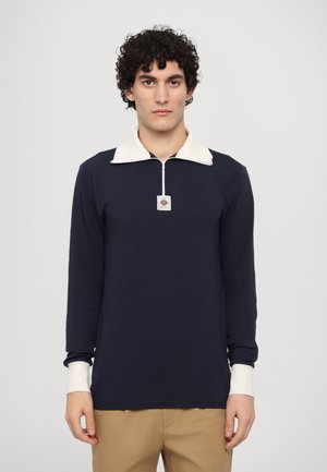 Navy long-sleeve polo shirt with a cream-colored collar and cuffs, featuring a quarter zipper and small emblem at the chest.