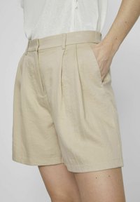 Béžové skládací šortky vyrobené z lehkého materiálu, s bočními kapsami a upraveným pasem. Hladká textura s uvolněným střihem.