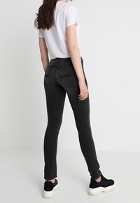 Svarta skinny jeans med hög midja, gjorda av denim. Bärs med en enkel vit T-shirt och svarta sneakers, vilket visar en figurnära siluett.