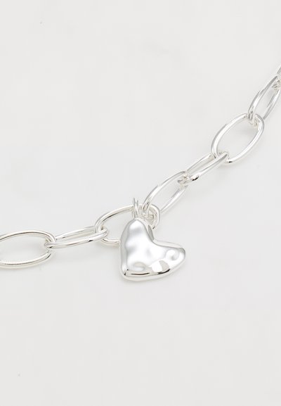Bracciale in argento con maglie ovali e un ciondolo a forma di cuore lucido, che riflette la luce grazie alla sua superficie liscia e lucente.