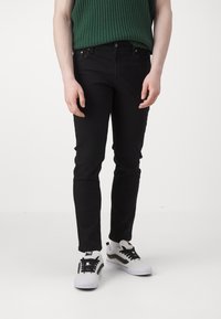 Czarne dżinsy w slim fit z przednimi kieszeniami i zapięciem na guzik. Dobrane z białymi trampkami i zielonym, prążkowanym topem.