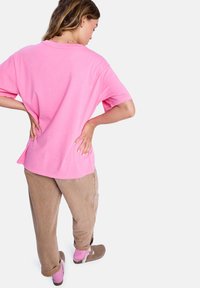 T-shirt rose oversize à manches courtes, associé à un pantalon beige clair ample et des chaussures slip-on marron. Chaussettes visibles en rose vif.