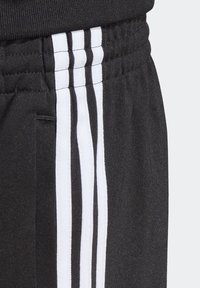 Shorts de sport noirs en tissu texturé, dotés d'une large ceinture élastique et de trois rayures verticales blanches sur le côté.