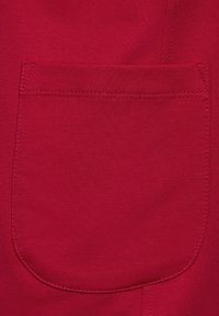 Tissu rouge avec une texture lisse présentant une grande poche arrière ronde, cousue sur les bords, offrant un détail fonctionnel.