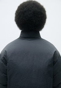 Dark padded jacket with a high collar, featuring a smooth, matte texture. The back displays subtle stitching details.