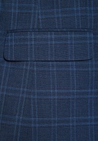 Granatowa tkanina w kratę z cienkimi niebieskimi liniami, o gładkiej fakturze. Zawiera prostokątną kieszeń z przeszytym brzegiem.