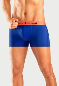 Blue boxer briefs with a snug fit, featuring an orange waistband with "bruno banani" logo. Material appears smooth and stretchy.