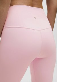 Light pink high-waisted leggings made from smooth, stretchy fabric feature subtle stitching and a logo detail at the back.