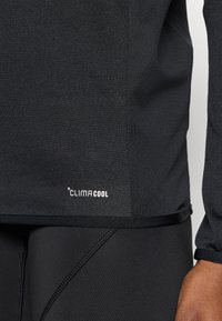 Μαύρο αθλητικό πουκάμισο με υφή, με λογότυπο CLIMACool σε λευκό. Ψηλός γιακάς και εφαρμ οστά μανίκια, συνδυασμένα με μαύρο κολάν που ταιριάζει.