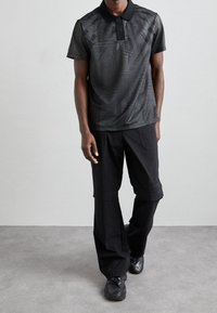Černé polo tričko s texturovaným vzorem, krátkými rukávy a límečkem; kombinováno s širokými černými cargo kalhotami; černé tenisky.