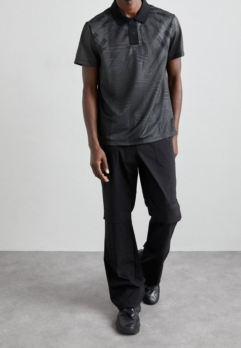 Černé polo tričko s texturovaným vzorem, krátkými rukávy a límečkem; kombinováno s širokými černými cargo kalhotami; černé tenisky.
