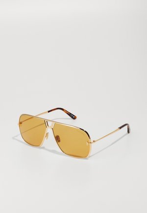 Lunettes de soleil en métal doré avec des verres ambrés ; forme géométrique avec un double pont, présentant des accents écaille de tortue brunes sur les branches.