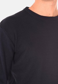 Pullover nero a costine con scollo rotondo e tessuto testurizzato. Ingrandimento che mette in evidenza il materiale e i dettagli del design.