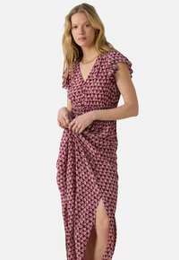 Robe bordeaux avec un imprimé floral, manches courtes volantées, décolleté en V profond, taille cintrée et design à fente sur le côté. Tissu léger, silhouette fluide.