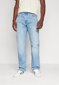 Jeanși din denim de culoare bleu deschis, cu croială dreaptă, având un design clasic cu cinci buzunare și o ușoară decolorare. Purtați cu adidași albi.