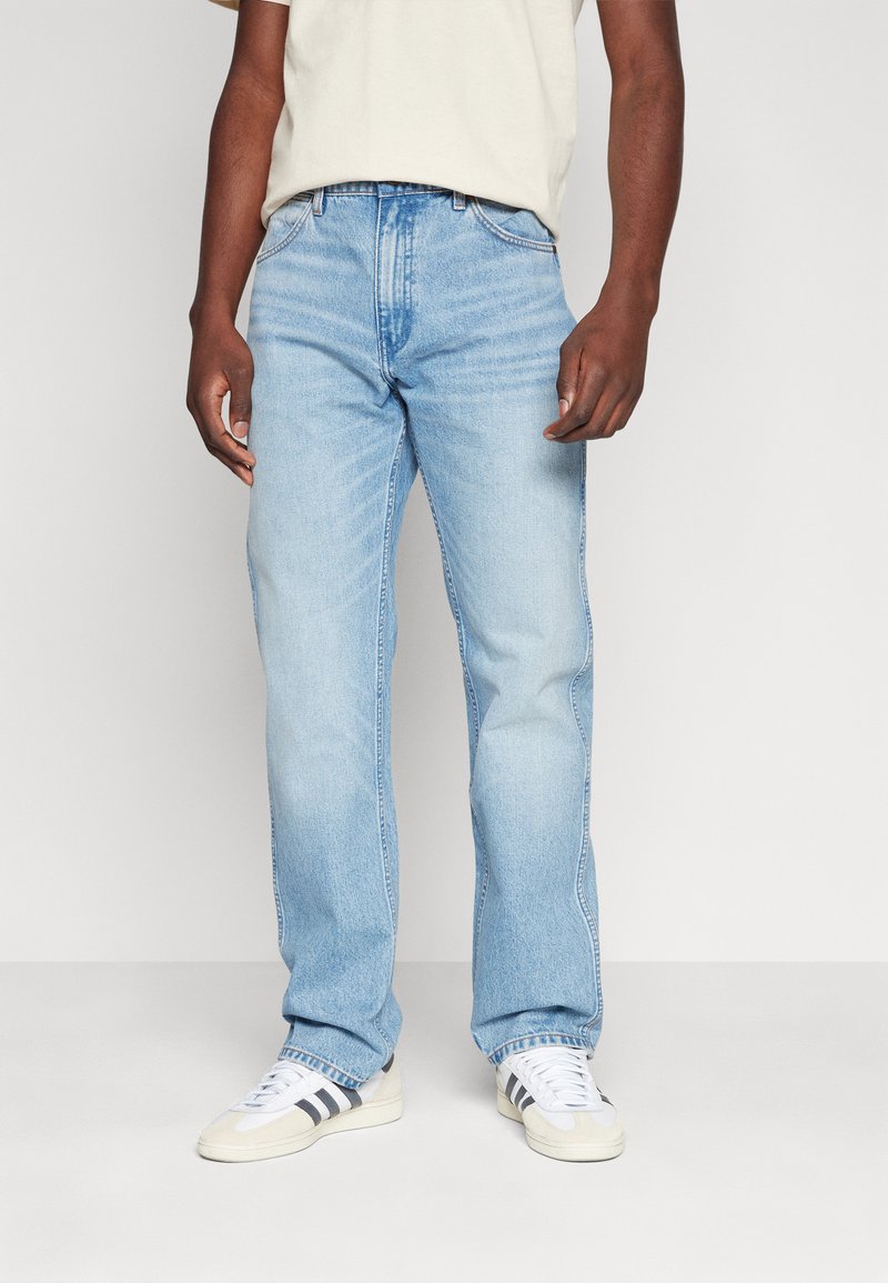Jeanși din denim de culoare bleu deschis, cu croială dreaptă, având un design clasic cu cinci buzunare și o ușoară decolorare. Purtați cu adidași albi.