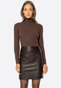 Dolcevita marrone abbinato a una mini gonna aderente in pelle nera. I materiali sono lisci con una finitura elegante e lucida.