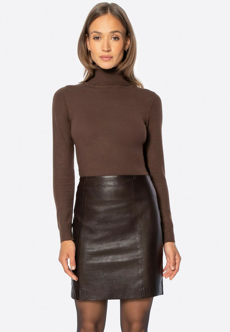 Dolcevita marrone abbinato a una mini gonna aderente in pelle nera. I materiali sono lisci con una finitura elegante e lucida.