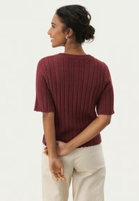 Pull en tricot bourgogne à manches courtes, avec un motif texturé de lignes verticales et un col et un ourlet côtelés.