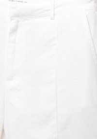 Pantalon en lin blanc avec une texture lisse, des poches latérales, et une coupe ajustée. Le tissu présente un motif de tissage subtil.