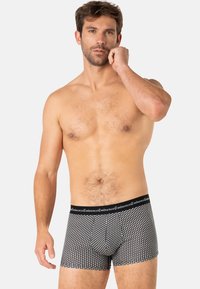 Boxers noirs avec un motif géométrique, taille élastique portant le nom de la marque. Tissu lisse, design ajusté, longueur mi-cuisse.