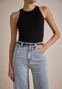 Top negro de canalé combinado con jeans de tiro alto en un tono azul claro. Los jeans presentan un diseño clásico de cinco bolsillos con un ligero desgastado.