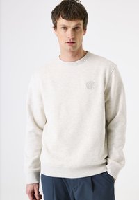 Lichtgrijze sweatshirt met een ronde halslijn en geribde mouwen, met een subtiel verdiept logo op de borst. Zacht, textuurstof.